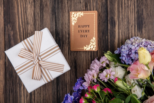 Draufsicht der erstaunlichen Blumen wie Fliederrosen-Gänseblümchen mit weißer Geschenkbox auf einem hölzernen Hintergrund