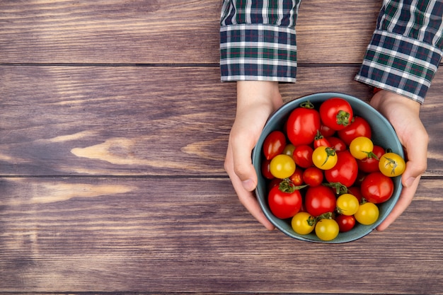 Draufsicht der Frauenhände, die Schüssel der Tomaten auf Holztisch halten