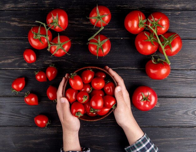 Draufsicht der Frauenhände, die Schüssel Tomaten mit anderen auf Holztisch halten