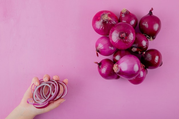 Kostenloses Foto draufsicht der frauenhand, die geschnittene zwiebel mit ganzen zwiebeln auf lila hintergrund mit kopienraum hält
