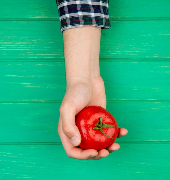 Kostenloses Foto draufsicht der frauenhand, die tomate auf grüner oberfläche hält