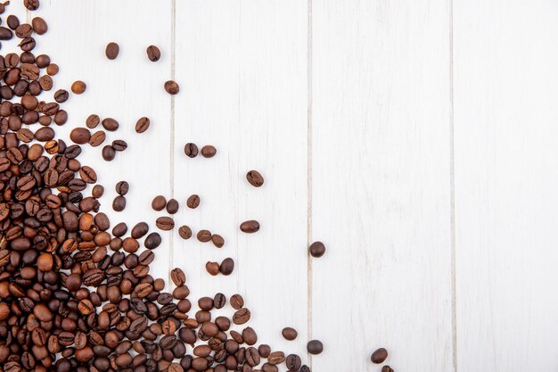 Draufsicht der frisch gerösteten Kaffeebohnen lokalisiert auf einem weißen hölzernen Hintergrund mit Kopienraum
