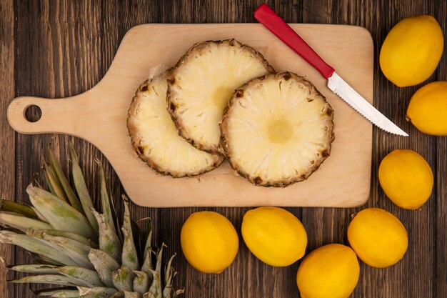 Kostenloses Foto draufsicht der frischen ananas auf einem hölzernen küchenbrett mit messer mit zitronen lokalisiert auf einer holzwand