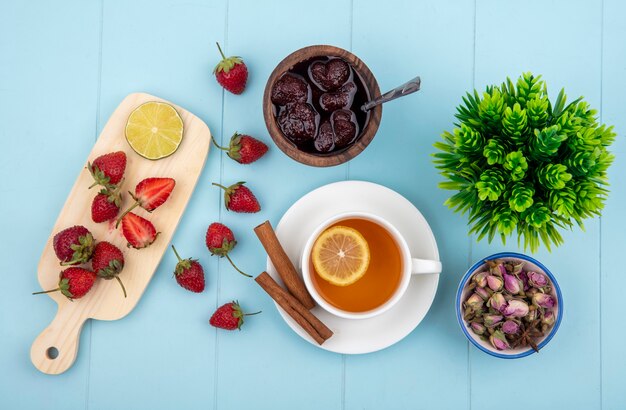 Draufsicht der frischen Erdbeere auf einem hölzernen Küchenbrett mit Kalk mit einer Erdbeermarmelade auf einer hölzernen Schüssel auf einem blauen Hintergrund