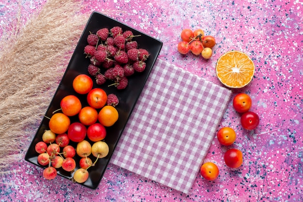 Draufsicht der frischen Früchte Himbeeren und Pflaumen innerhalb der schwarzen Form auf der rosa Oberfläche