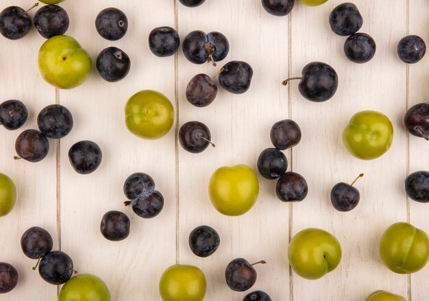 Draufsicht der frischen Früchte wie grüne Kirschpflaume und dunkelviolette Schlehen lokalisiert auf einem weißen hölzernen Hintergrund