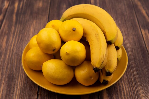 Draufsicht der frischen gelbhäutigen Zitronen auf einem gelben Teller mit Bananen auf einer Holzoberfläche