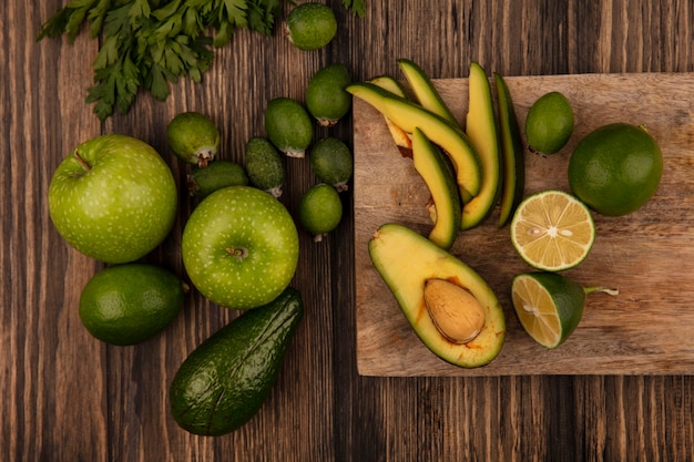 Draufsicht der frischen halben Avocado mit Scheiben auf einem hölzernen Küchenbrett mit Äpfeln feijoas Kalk und Petersilie lokalisiert auf einer hölzernen Oberfläche