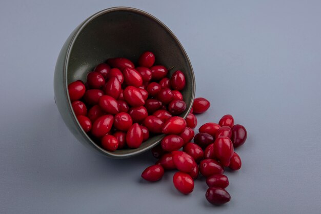 Draufsicht der frischen Kornelkirschenbeeren, die die Schüssel auf einem grauen Hintergrund herausfallen