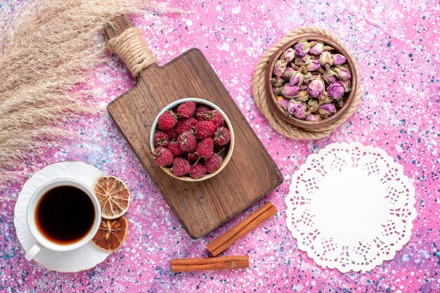 Draufsicht der frischen leckeren Himbeeren innerhalb des weißen Tellers mit Tee und Zimt auf der rosa Oberfläche