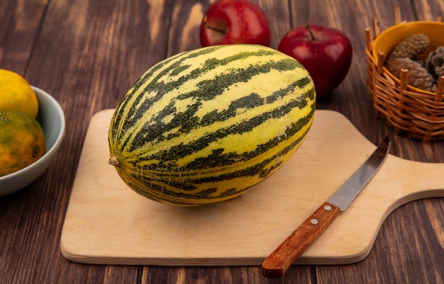 Kostenloses Foto draufsicht der frischen melone melone auf einem hölzernen küchenbrett mit messer mit äpfeln lokalisiert auf einer holzwand