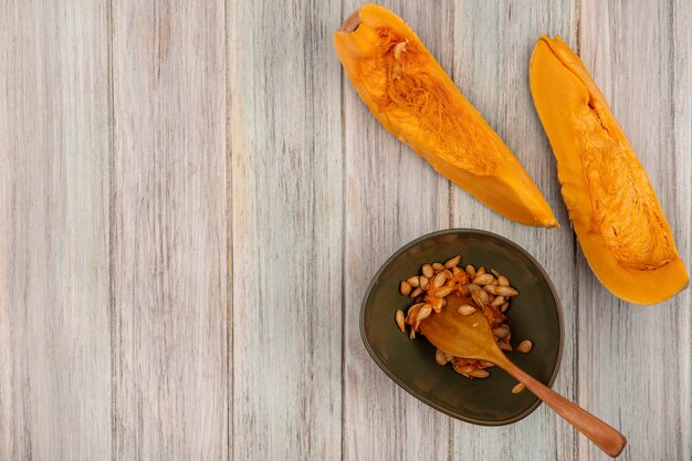 Draufsicht der frischen orange Kürbisscheiben mit Samen auf einer Schüssel mit Holzlöffel auf einer grauen Holzwand mit Kopienraum