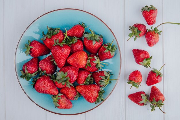 Draufsicht der frischen reifen Erdbeeren auf einem blauen Teller auf weißer Oberfläche