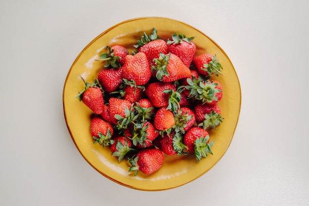 Draufsicht der frischen reifen Erdbeeren in einem gelben Teller auf Weiß