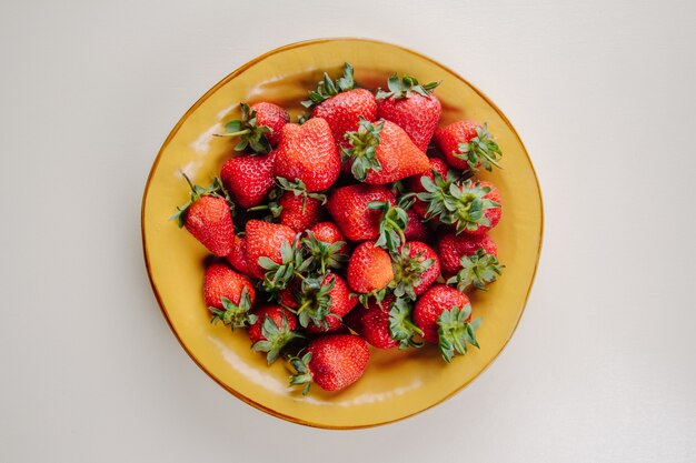 Draufsicht der frischen reifen Erdbeeren in einem gelben Teller auf Weiß