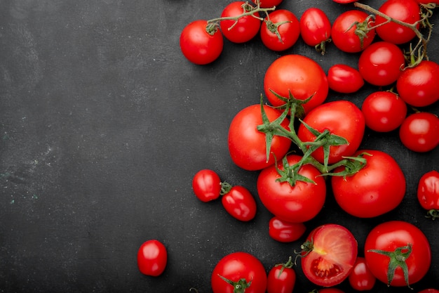 Draufsicht der frischen reifen Tomaten verstreut auf schwarzem Hintergrund mit Kopienraum