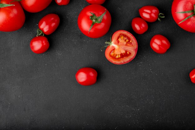 Draufsicht der frischen reifen Tomaten verstreut auf schwarzem Hintergrund mit Kopienraum