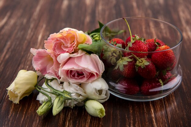 Draufsicht der frischen roten Erdbeeren auf einer Schüssel mit schönen Blumen wie Tulpe und Rosen auf einem hölzernen Hintergrund