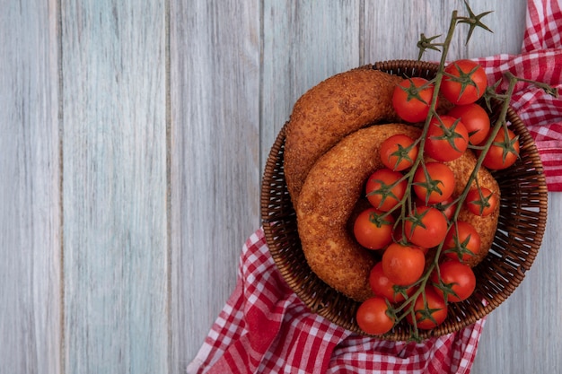 Draufsicht der frischen roten tomaten auf einem eimer mit bagels auf einem sackstoff auf einem grauen hölzernen hintergrund mit kopienraum