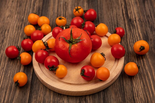 Draufsicht der frischen roten und orange Tomaten lokalisiert auf einem hölzernen Küchenbrett auf einer Holzwand