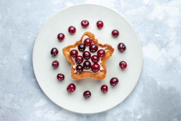 Draufsicht der frischen Sauerkirschen innerhalb der Platte mit sternförmigem Kuchen auf hellweißem Schreibtisch, Fruchtsauerbeeren-Vitaminsommer