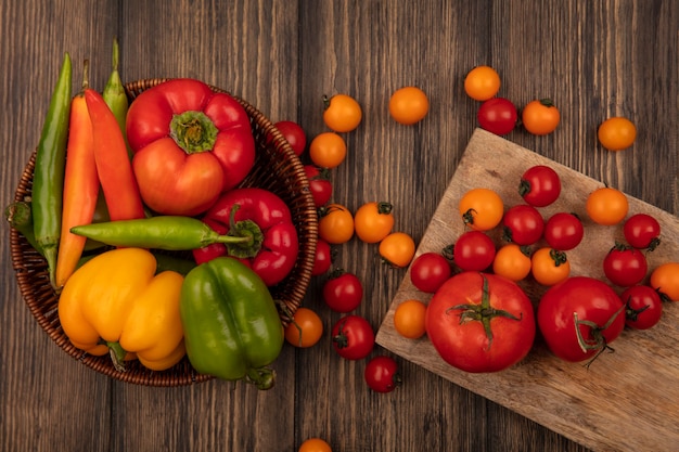 Draufsicht der frischen Tomaten lokalisiert auf einem hölzernen Küchenbrett mit bunten Paprikaschoten auf einem Eimer auf einer Holzwand