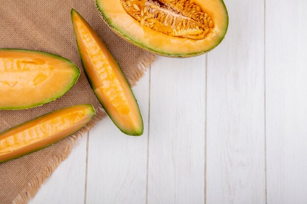 Draufsicht der frischen und gesunden Melone Melone mit Scheiben auf Sack Stoff auf Weiß