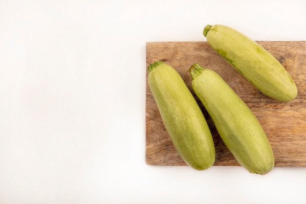 Draufsicht der frischen Zucchini lokalisiert auf einem hölzernen Küchenbrett auf einer weißen Oberfläche mit Kopienraum