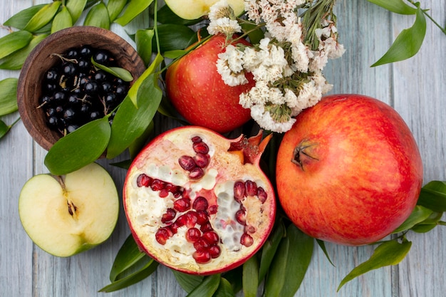 Draufsicht der Früchte als Granatapfel- und Apfelhälften mit ganzen und Schale des Schwarzdorns mit Blumen und Blättern auf schwarzer Oberfläche