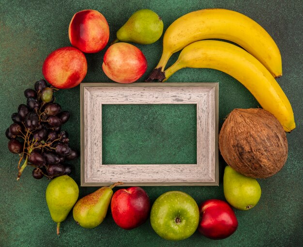 Draufsicht der Früchte als Pfirsich-Kokosnuss-Apfel-Birnen-Bananen-Traube um Rahmen auf grünem Hintergrund mit Kopienraum