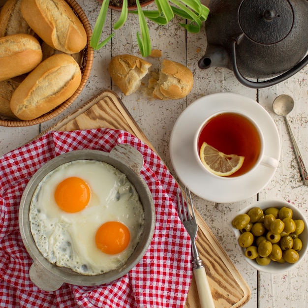 Draufsicht der Frühstückseinrichtung mit Eiern, Oliven, Brot und schwarzem Tee