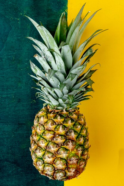 Draufsicht der ganzen Ananas auf grüner und gelber Oberfläche