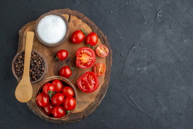 Draufsicht der ganzen geschnittenen frischen Tomaten und des Pfeffers auf Holzbrett auf schwarzer Oberfläche