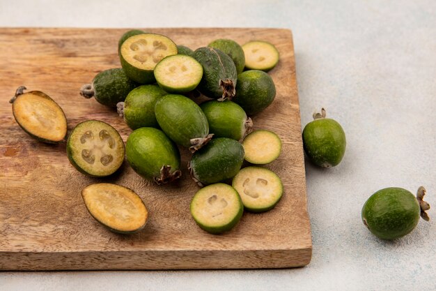 Draufsicht der ganzen und halbierten frischen feijoas lokalisiert auf einem hölzernen Küchenbrett auf einem grauen Hintergrund