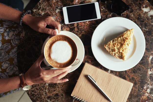 Draufsicht der geernteten unerkennbaren Frau, die Kaffee und Nachtisch im Café trinkt