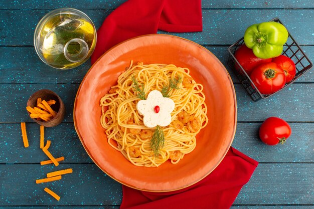 Draufsicht der gekochten italienischen Nudeln mit Grüns innerhalb des orangefarbenen Tellers mit Öl und Gemüse auf der blauen Holzoberfläche