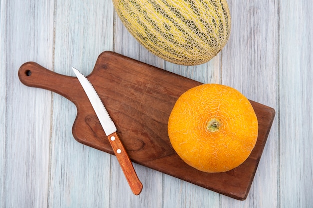 Draufsicht der gelben köstlichen Melone auf einem hölzernen Küchenbrett mit Messer auf einer grauen Holzoberfläche