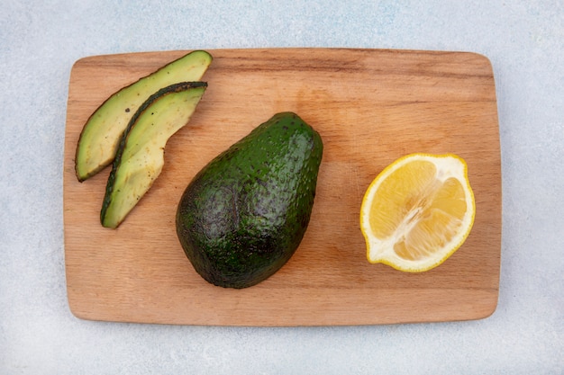 Draufsicht der gesunden frischen Avocado auf einem hölzernen Küchenbrett mit Zitrone auf weißer Oberfläche