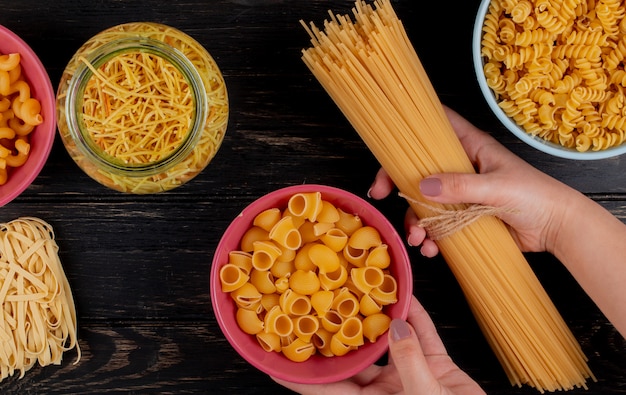 Draufsicht der Hände, die Fadennudeln mit verschiedenen Arten von Nudeln als Cavatappi Rotini Tagliatelle und Spaghetti auf Holzoberfläche halten