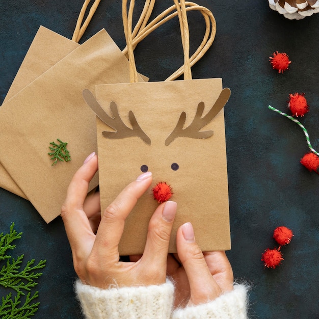 Draufsicht der Hände, die niedliche Rentierweihnachtsgeschenktüten verzieren