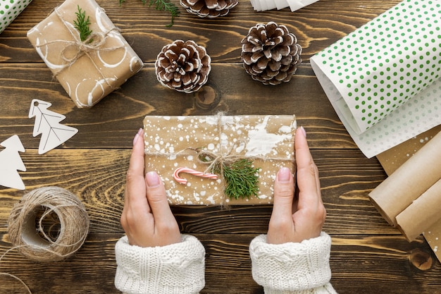 Kostenloses Foto draufsicht der hände, die weihnachtsgeschenk mit schnur und tannenzapfen halten