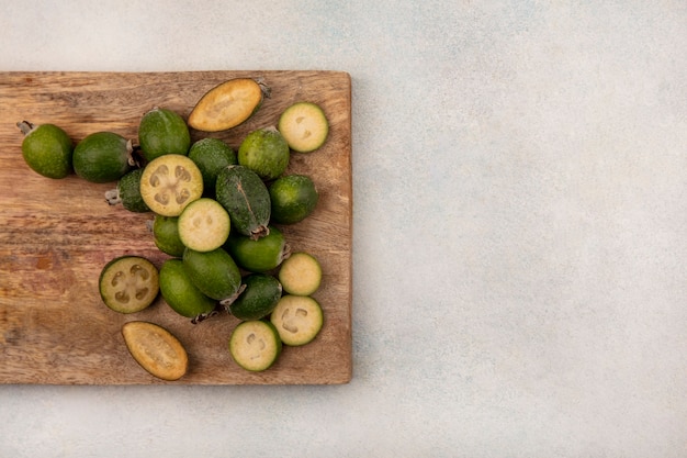 Draufsicht der halben und ganzen feijoas lokalisiert auf einem hölzernen Küchenbrett auf einem grauen Hintergrund mit Kopienraum