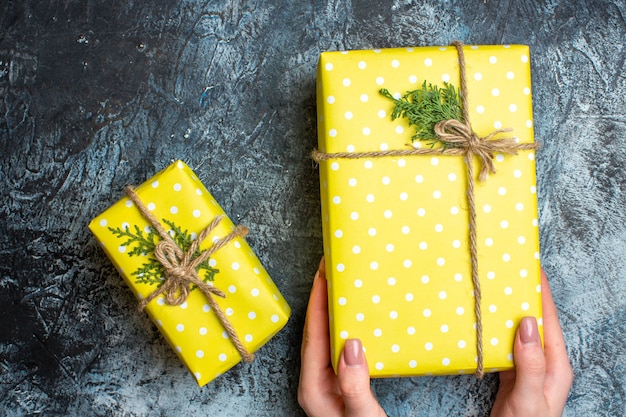 Kostenloses Foto draufsicht der hand, die eine der weihnachtlichen gelben geschenkboxen auf dunklem hintergrund hält