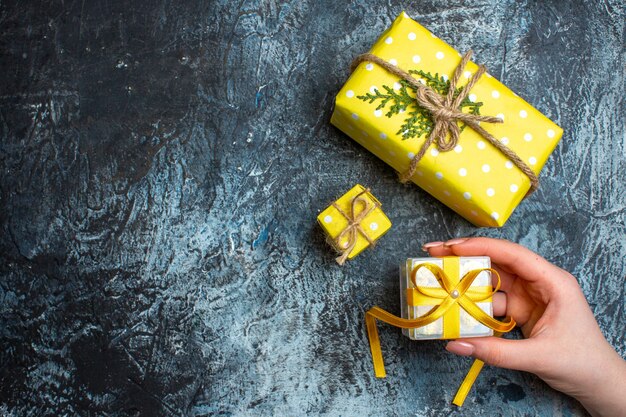 Draufsicht der Hand, die eine kleine Geschenkbox und andere zwei Weihnachtsgeschenkboxen auf dunklem Hintergrund öffnet