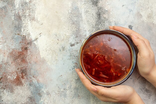 Draufsicht der Hand, die einen blauen Topf mit köstlicher Borschtsch-Suppe auf einem bunten Hintergrund hält