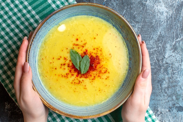 Draufsicht der Hand, die einen blauen Topf mit leckerer Suppe hält, serviert mit Minze und Pfeffer auf blauem Hintergrund