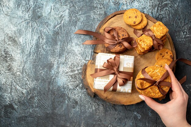 Draufsicht der Hand, die einen von verschiedenen leckeren Keksen auf einem Holzschneidebrett auf der linken Seite auf dunklem, eisigem Hintergrund hält