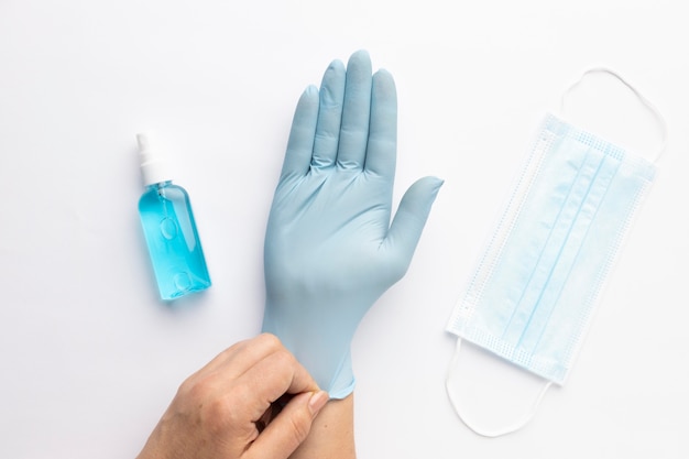 Draufsicht der Hand, die Handschuh mit Händedesinfektionsmittel und medizinischer Maske anzieht