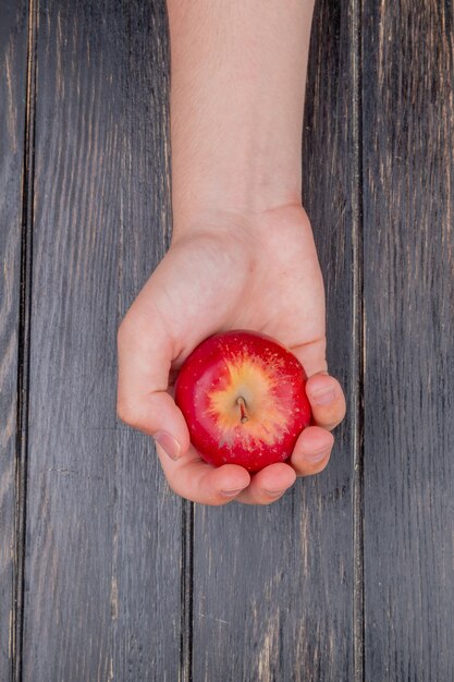 Draufsicht der Hand, die roten Apfel auf Holztisch hält