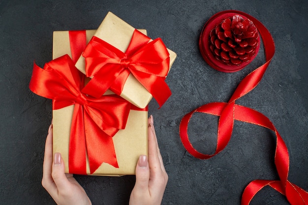 Draufsicht der Hand, die schöne Geschenke und Nadelbaumkegel auf dunklem Hintergrund hält